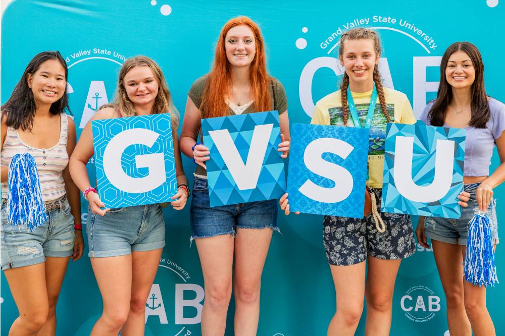 students posing in front of CAB backdrop holding GVSU letters at Laker Kickoff photo booth